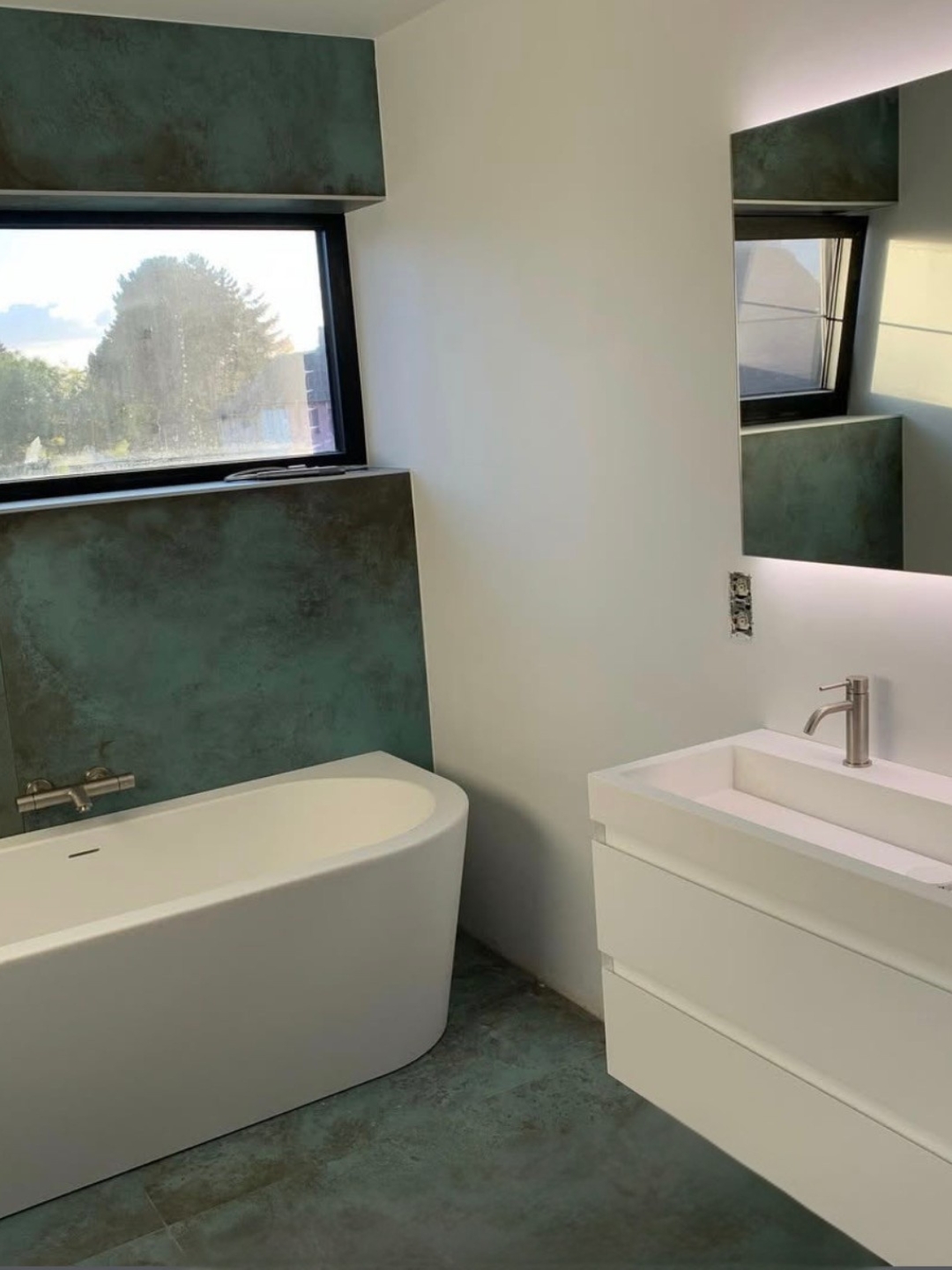 Moderne badkamer met een wit vrijstaand ligbad, wit wastafelmeubel en kopergroene accentwanden