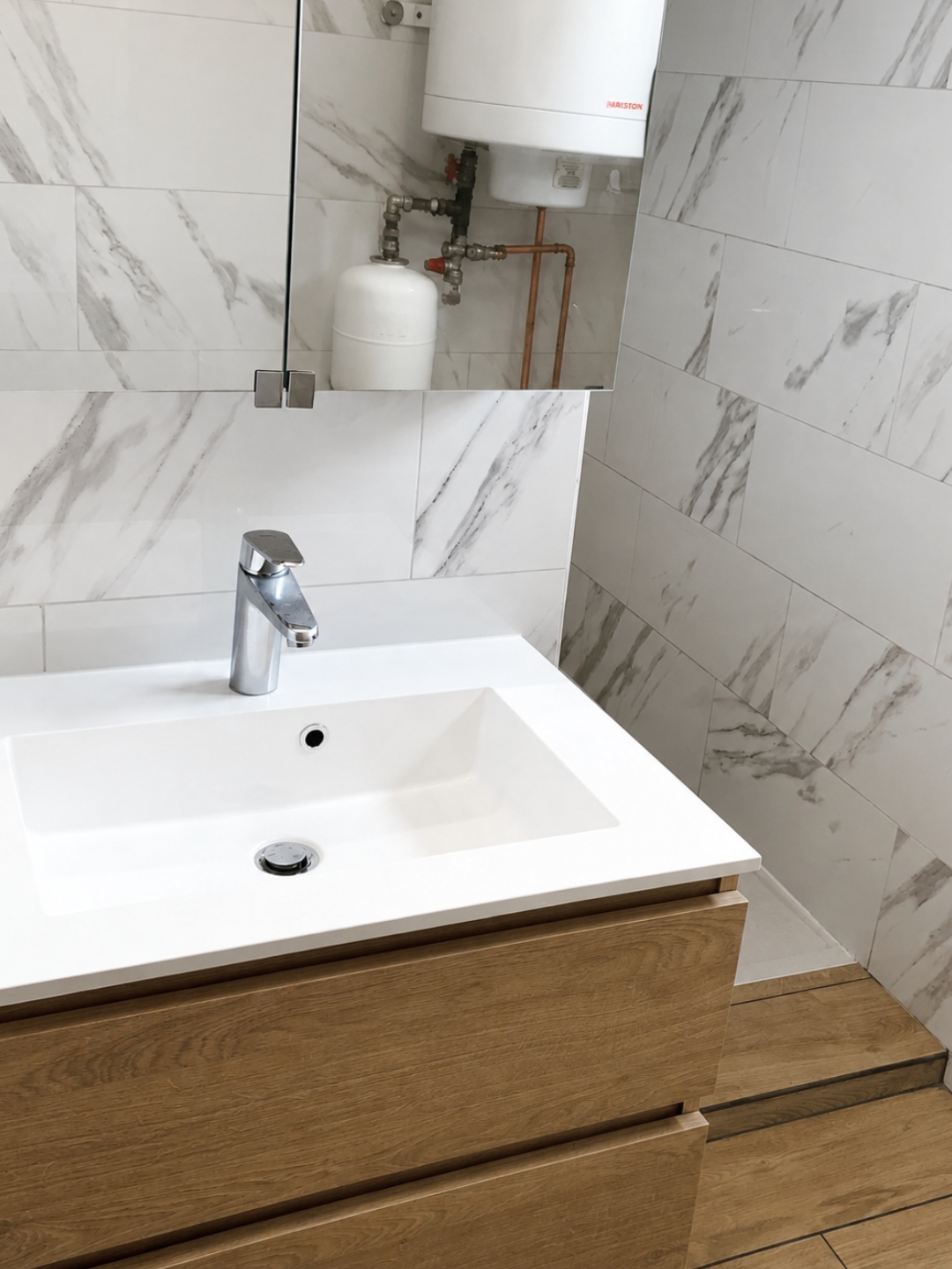 Moderne badkamerwastafel van licht hout met witte waskom en spiegelkast tegen een marmerlook tegelwand